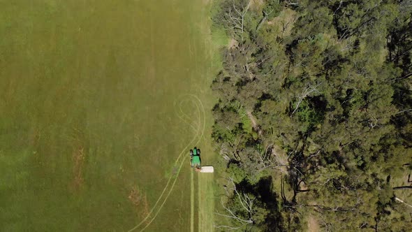 A birds eye view aerial of a tractor cutting dry grass alongside bushland in rural Australia.