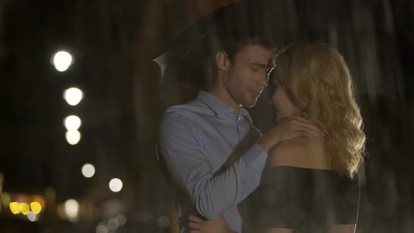 Man petting his blond girlfriend under the rain, couple waiting for taxi, love