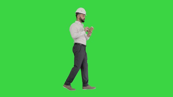 Confident Mature Man in Formalwear and Hardhat Writing Down Notes on a Green Screen, Chroma Key.