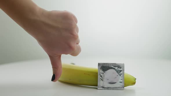 Closeup Contraceptive and Banana at White Background with Female Hand Gesturing Thumb Down