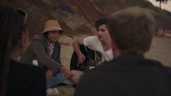 Young Cheerful Friends Sitting By the Fire on the Beach in the Evening Cooking Marshmallow and