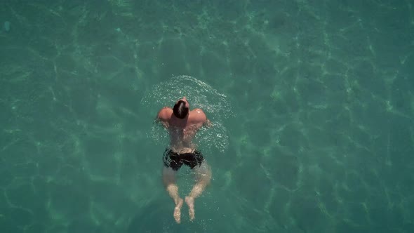 Aerial view of a man swimming in transparent water in Syros island, Greece.