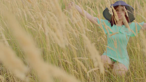 Young Woman in Dress and Hat Sitting in Wheat Field