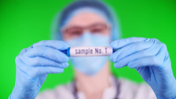 Green Background. Close-up, Doctor's Hands in Blue Medical Gloves Holds Test Tube with Inscription