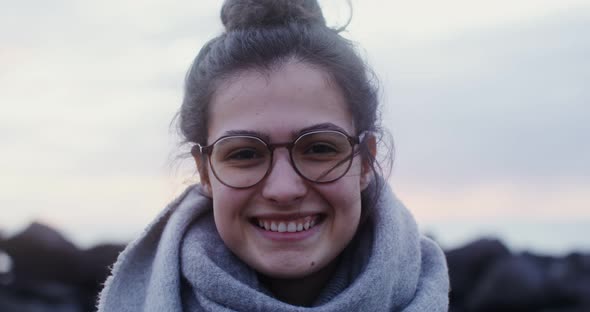 A Young Woman in Glasses with a Laughs Looking at the Camera on the Seacoast