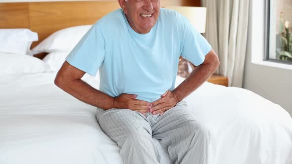 Senior man sitting on bed with a stomach ache