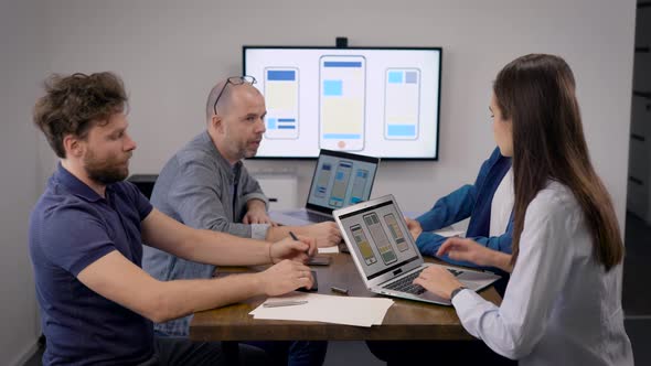 Team of Developers of Mobile Apps Is Working in Office Room at Meeting, Talking