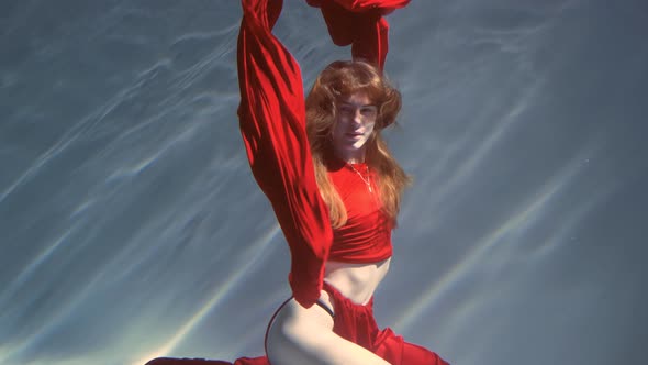 Attractive Redhaired Young Woman Swims Beautifully Underwater in a Red Dress