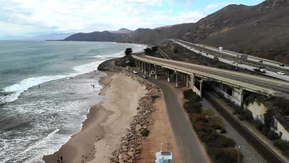 Aerial drone shot orbiting around a concrete bridge on the beach in Ventura with surfers in the ocea