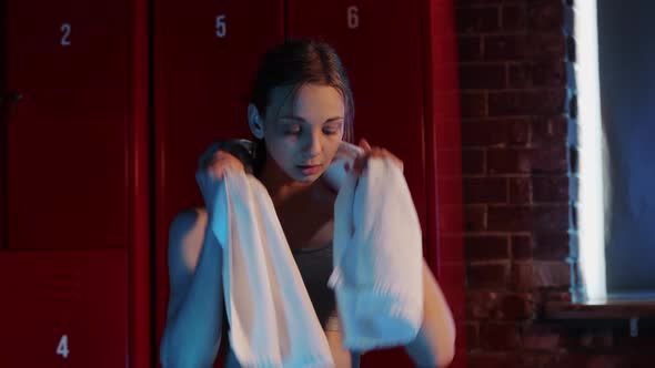 Sports  Young Woman Sitting in Locker Room and Putting a Towel on Her Neck