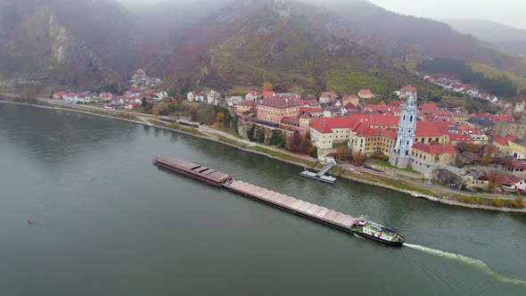 Cargo Pusher Boat on a River Transporting Cargo and Goods Past a Town