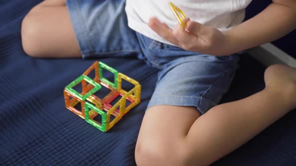 Boy Child in a White Tshirt is Sitting on a Bed Against a Blue Wall and Playing