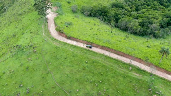 Aerial View of Car Driving Throuh a Small Dirt Road in the Middle of Green Tropical Valley.