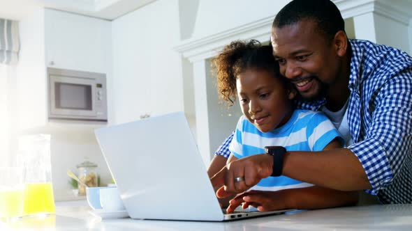 Father and daughter using laptop in kitchen