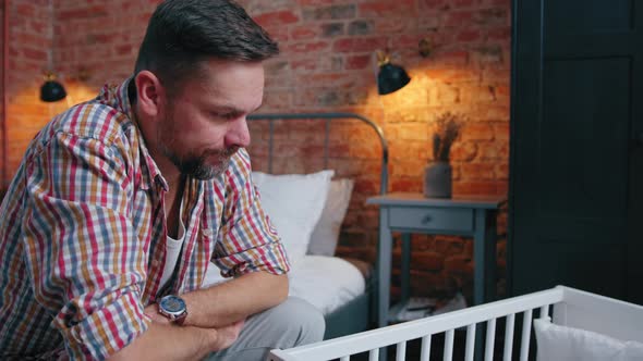 Novice Dad Sitting Next to the Cradle Feeling Terrified About His Infant Baby's Future