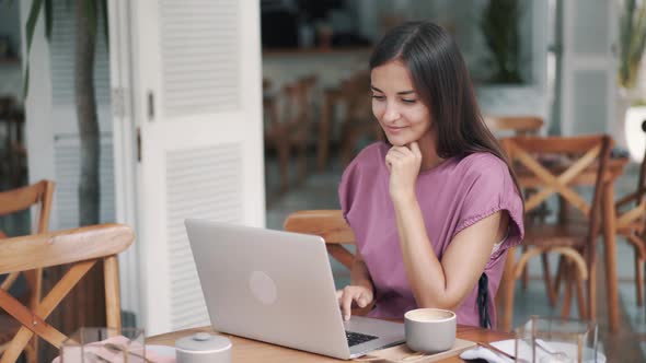 Portrait of Woman Freelancer Sitting at Table and Using Laptop for Work in Cafe