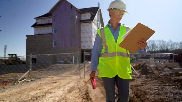 Wide angle closeup shot from ground of woman engineer on large building construction site walking to