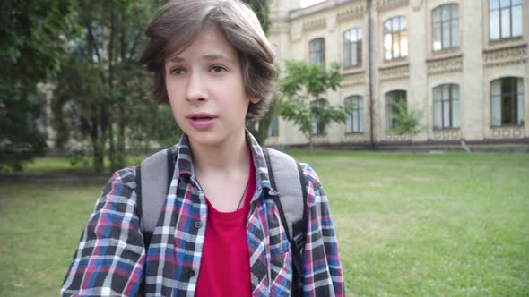 Aggressive Brunette Schoolboy Pointing and Talking at Camera Outdoors. Portrait of Cute Caucasian