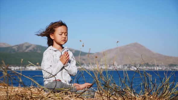 Cute Little Child Gurl Meditating Alone in Lotus Pose at Lake Shore