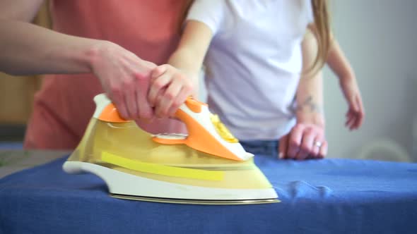 Mom and Cute Daughter Ironing Clean Clothes and Standing in Apartment Room Spbd