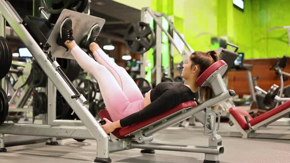 Side View of Fit Young Sportswoman Flexing Her Leg's Muscles on Exercise Machine at the Gym