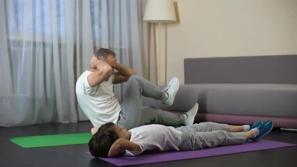 Father With Son Doing Abdominal Crunches at Home, Showing Benefit of Sports