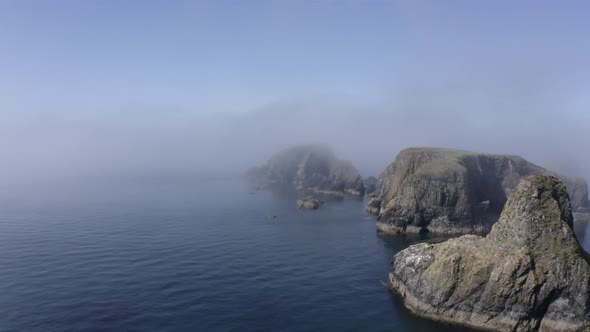 Seashore aerial flies into afternoon fog on jagged ocean rock islets