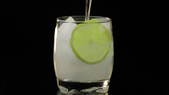 A Refreshing Drink Being Poured Into a Glass with Ice, and Lime