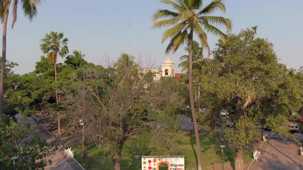 Flyover Jardín Núñez Overlooking Templo de la Merced At Background In Colima City, Mexico. Aerial Dr