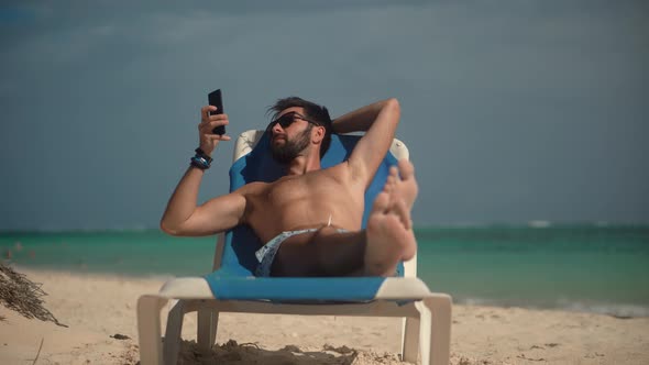 Tan Man Relaxing On Vacation Caribbean Tropical Beach. Beautiful Man Lies On Sunbed On Vacation.