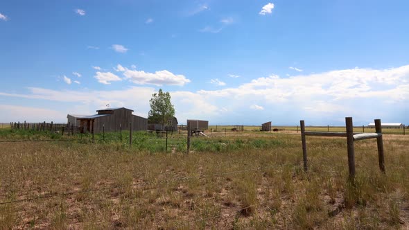 An old time western barn with a corral and weather vein stands century over a barren plain while puf