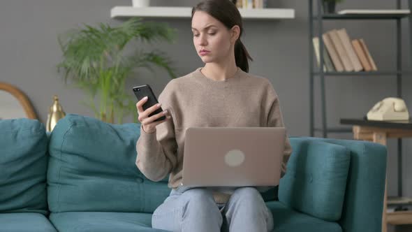 Woman with Laptop Using Smartphone on Sofa