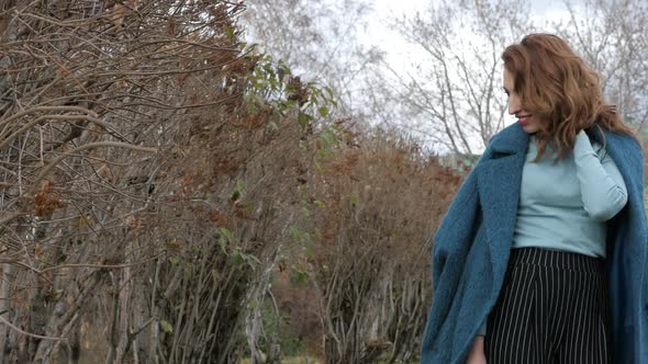 Young Redhaired Woman in a Blue Coat and Walks Against the Backdrop of the Old City