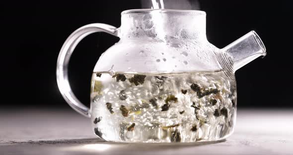 Process of Brewing Herbal Tea in Glass Transparent Teapot at Dark Background