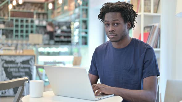 African Man with Laptop Pointing at Camera in Cafe
