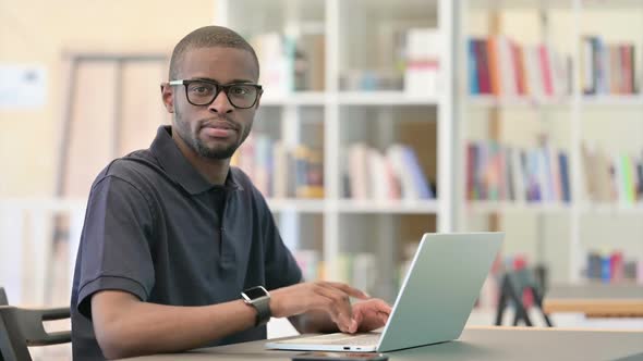 Cheerful Young African Man Pointing with Finger in Library