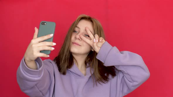 Attractive cheerful Caucasian young woman over 20 in casual sportswear takes a selfie on a smartphon