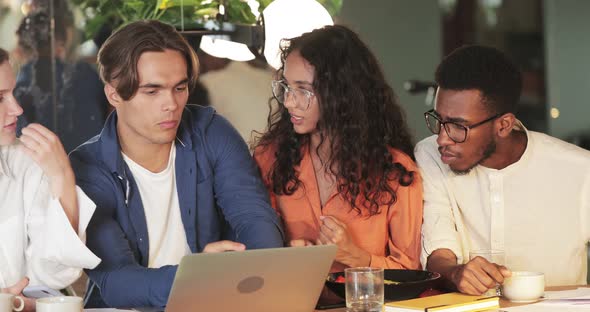 Crop View of Millennial Colleagues Looking at Laptop Screen While Sitting in Cafe. Cheerful Diverse