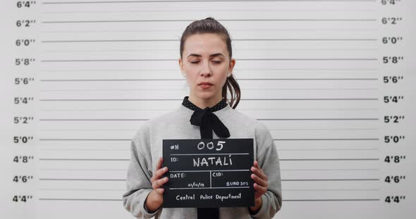 Portrait of Young Woman with Ponytail Holding Sign for Photo in Police Department