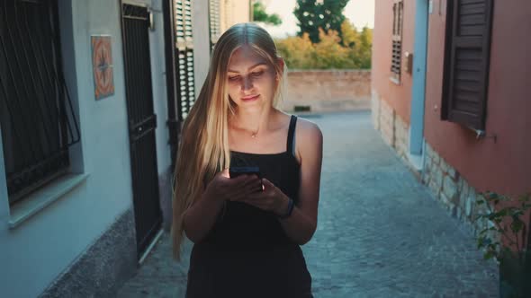 Woman Reading Something on Smartphone While Walking the Street