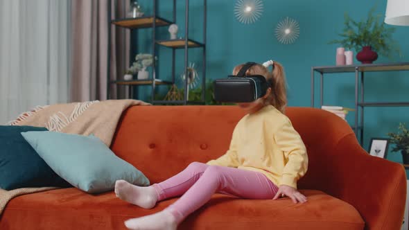 Toddler Girl Sitting on Home Sofa Using Virtual Reality Headset Helmet App to Play Video 3D Game