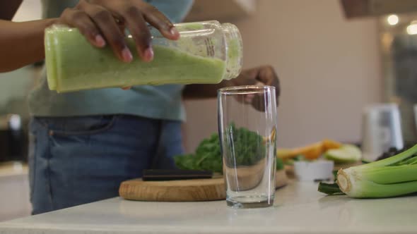 Hands of african american attractive woman pouring homemade smoothie into glass in kitchen