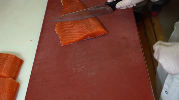 Chef cutting smoked salmon fillets and sliding it off to nearby table - top down view