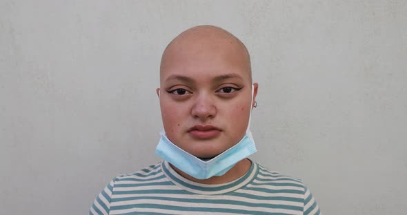 Bald girl posing in front of camera while wearing safety face mask under chin