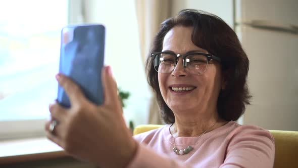 Woman Having Online Talk and Waving in Front of Smartphone Screen in Apartment Room