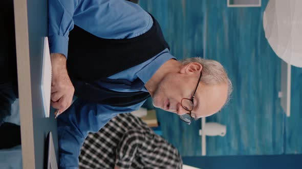 Vertical Video Multitasking Retired Man Reading on Laptop and Writing on Notebook