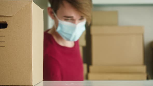 Man Wearing Medical Face Mask and Protective Gloves Putting Parcel on Shelf Employee of Warehouse