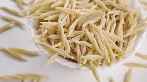 Italian uncooked dry trofie pasta falling into white bowl in slow motion. Rotation