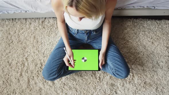 Woman in Jeans Sits in Lotus Position on Floor and Uses Electronic Tablet with Green Screen Top View