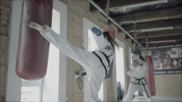 Two Taekwondo Girls Train For A Kick Into Punching Bag